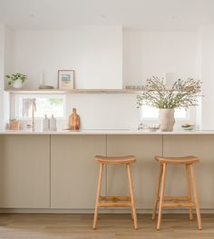 two wooden stools sit in front of an island with white countertops and cabinets