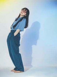 a woman standing in front of a white wall wearing sunglasses and a blue jumpsuit