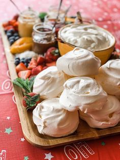 a wooden platter filled with whipped cream and fruit on top of a red table cloth