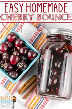 a jar filled with cherries sitting on top of a table next to cinnamon sticks