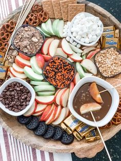 an assortment of snacks are arranged on a platter with pretzels, apple slices and chocolate