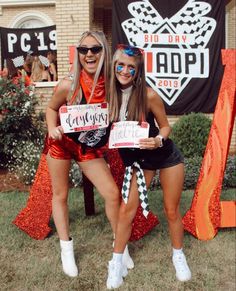 two women in costumes posing for the camera with signs on their shoulders and legs, both wearing sunglasses