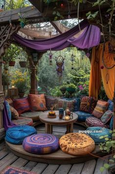 an outdoor living area with lots of pillows on the floor and colorful curtains hanging from the ceiling