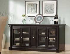 a sideboard with glass doors and two pictures on the wall