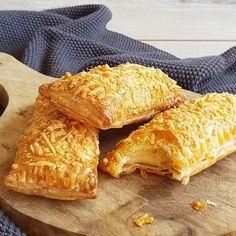 three pastries on a wooden cutting board next to a cup of coffee and blue towel