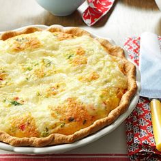 a quiche with cheese and vegetables in a white dish on a red and white tablecloth