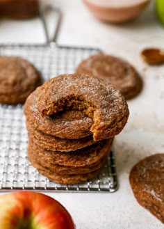 a stack of cookies sitting on top of a cooling rack with an apple in the background