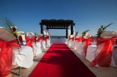 a red carpeted aisle with white and red sashes is lined up on the beach