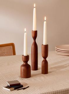 three candles are sitting on a table with plates and napkins in front of them