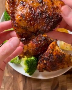 two hands are holding up some food on a plate with broccoli and chicken