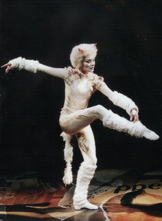 a man dressed in white doing a trick on the dance floor with his arms outstretched