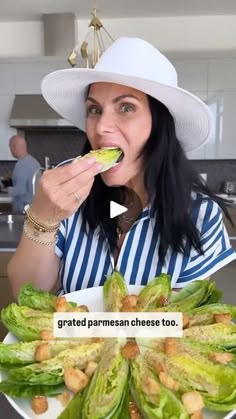 a woman in a white hat is eating some lettuce and has her mouth open