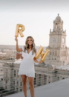 a woman in white dress holding up gold letter balloons