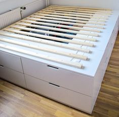 a white bed with drawers underneath it in a room that has wood floors and hard wood flooring