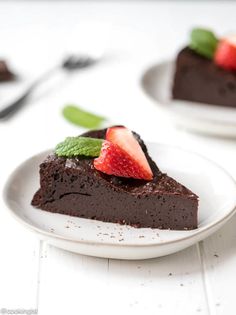 a piece of chocolate cake on a plate with strawberries and mint leaves in the middle