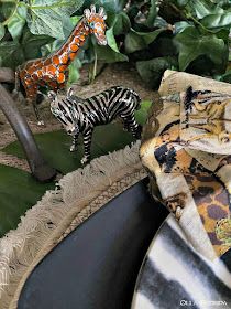 two zebra figurines sitting on top of a table next to green leaves and plants