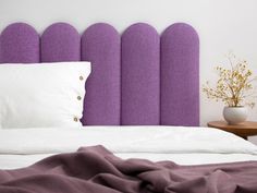 a bed with purple headboard next to a white pillow and vase on top of it