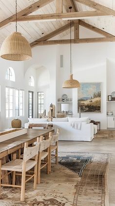 a large open living and dining room area with wood beams on the ceiling, white couches, wooden chairs, and rugs