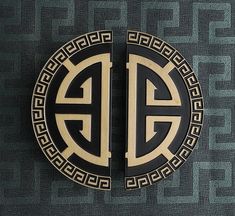 two black and gold emblems on the side of a gray wall with greek ornament designs