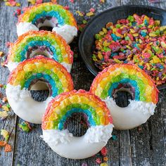 four rainbow donuts with sprinkles on them and a bowl of cereal in the background