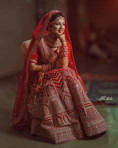 a woman in a red and white bridal dress sitting on a chair with her hands clasped