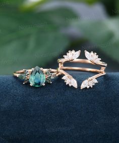 two gold rings with green and white stones on them sitting on a blue velvet surface