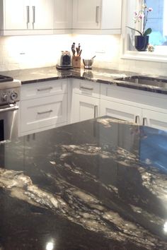 a kitchen with marble counter tops and white cabinets, along with stainless steel stove top oven