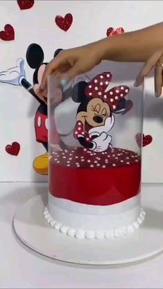 a person touching the top of a cake with minnie mouse on it