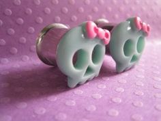 two green and pink hello kitty ear plugs on a purple background with polka dots