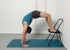 a man doing a handstand on a blue mat in front of a chair