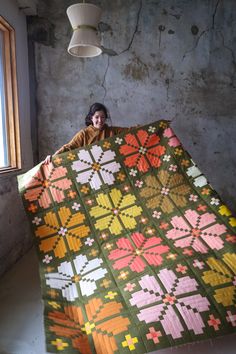 a woman is holding up a quilt in an old room with concrete walls and flooring