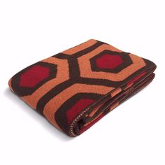 a brown and red blanket on top of a white surface with an orange design in the middle