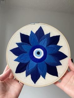 a person holding up a blue and white embroidered object with an evil eye in the center