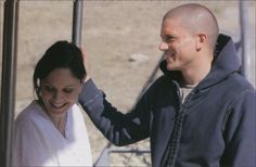 a man standing next to a woman in front of a metal fence with his hand on her head