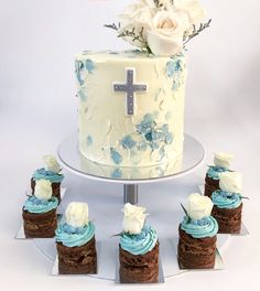 a cake with blue frosting and white flowers on top is surrounded by small cupcakes