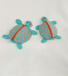 two sea turtle brooches are sitting on a white surface together, one is blue and the other is orange