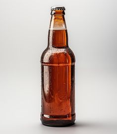 a brown beer bottle with water droplets on the top and bottom, sitting in front of a white background