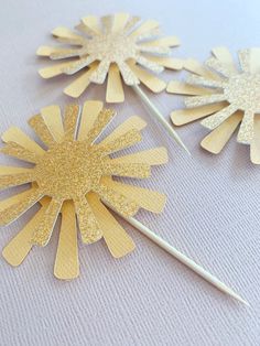 gold paper flowers are sitting on top of a white tablecloth and one has a toothpick sticking out of it