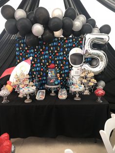 an astronaut themed birthday party with balloon decorations and black table cloths, including the number five