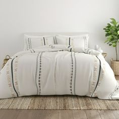 a bed with white sheets and pillows in a room next to a potted plant