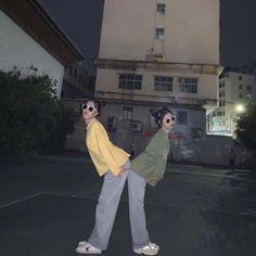 two people standing in front of a building at night with their arms around each other