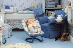 there is a baby doll sitting in a blue rocking chair next to a teddy bear