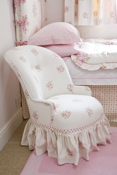 a white chair sitting next to a bed in a room with pink walls and curtains