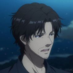 a man with black hair and blue eyes staring at the camera while standing in front of an ocean