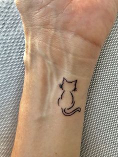 a cat tattoo on the wrist of a woman's hand, with black ink