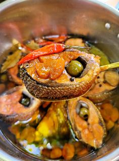 a spoon with some food in it on top of a pot filled with water and vegetables