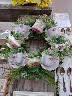 a wreath made out of teacups and greenery is displayed on a table