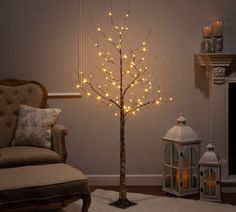 a lighted tree in a living room next to a chair