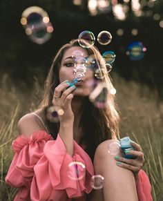 a woman sitting in the grass blowing bubbles