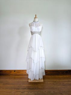 a white dress on a mannequin stand in front of a wall and wooden floor